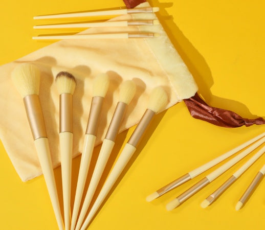 13Pcs Makeup Brush Set with beige handles and soft bristles, includes concealer, blush, powder, and eyeshadow brushes with pouch on yellow background.