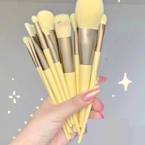 Hand holding 13Pcs Makeup Brush Set with yellow handles and gold ferrules, featuring powder, blush, and eyeshadow brushes for cosmetic application.